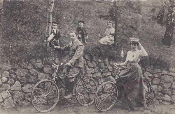  - rodina se třemi dětmi, děti sedíci na trávě, muž a žena sedící na kolech